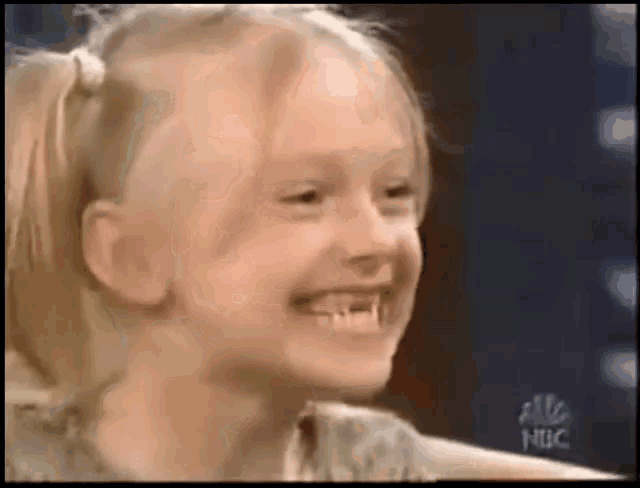 a little girl with pigtails is smiling with a nbc logo in the background