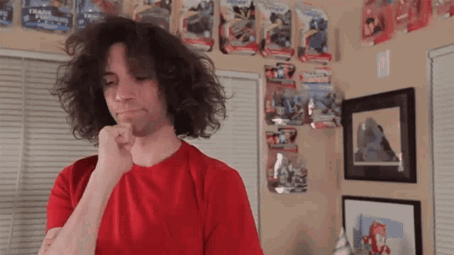 a man in a red shirt is standing in front of a wall with transformers toys on it
