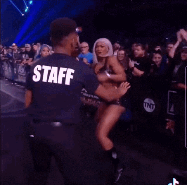 a woman in a black top and shorts is dancing in front of a crowd with aew written on the wall