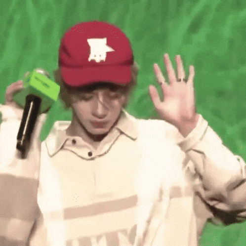 a young man wearing a red hat and a white shirt is holding a microphone .