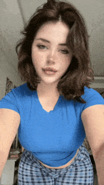 a woman wearing a blue shirt and plaid pants takes a selfie