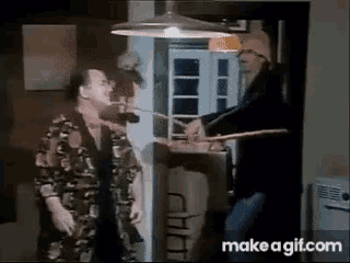a man is standing next to another man in a kitchen holding a sword .