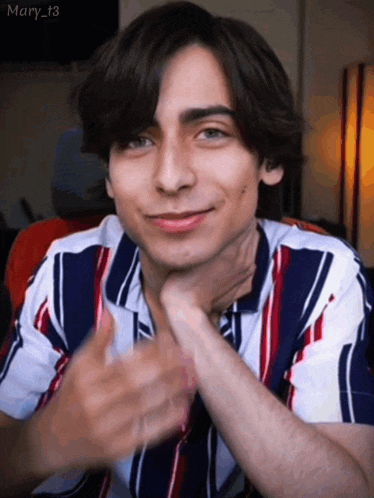 a young man wearing a striped shirt is smiling with his hands folded .