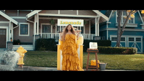 a woman in a yellow dress stands in front of a lemonade stand in front of a house
