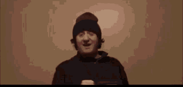a man wearing a beanie is making a funny face in a dark room .