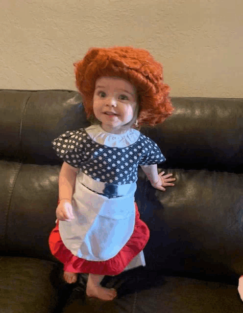 a little girl wearing a polka dot dress and apron is standing on a couch