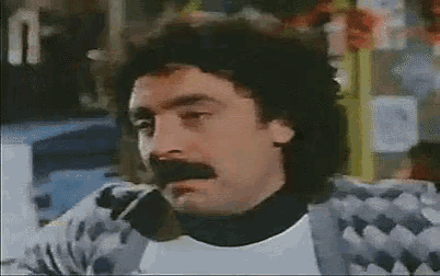a man with a mustache is smoking a cigarette and looking at the camera .