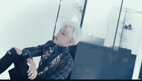 a man with white hair is sitting on the floor wearing a plaid jacket