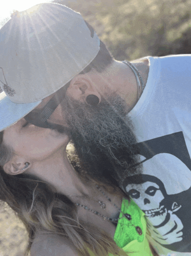 a man with a beard is kissing a woman who is wearing a shirt that says misfits