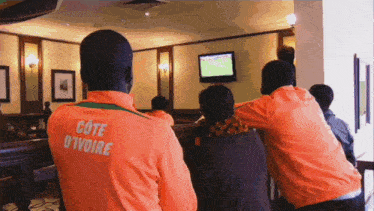 a man in an orange cote d' ivoire jacket watches a game