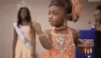 a little girl in a dress is standing next to another little girl in a sash .