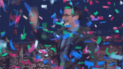 a man in a suit and tie is standing in front of a crowd while confetti is falling around him .