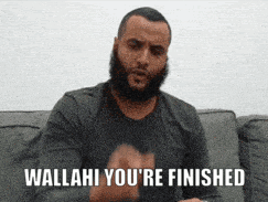 a man with a beard is sitting on a couch and says wallahi you 're finished .