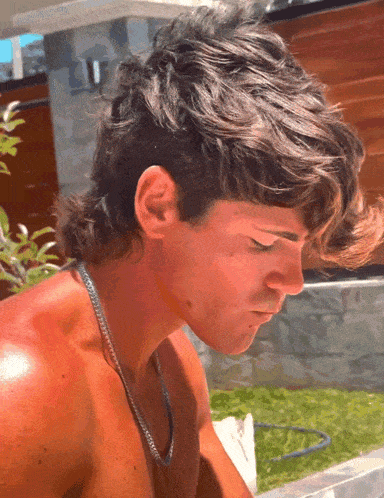 a shirtless man with a necklace around his neck looks down at something