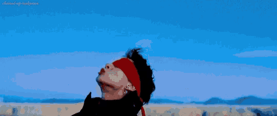 a man wearing a red headband and a black jacket is standing in front of a blue sky .