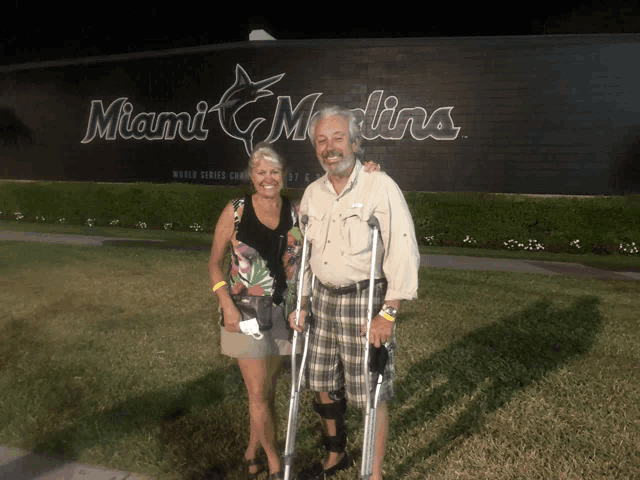 a man with crutches stands next to a woman in front of a miami marlins sign