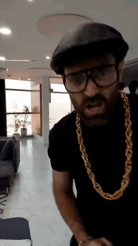 a man wearing glasses and a gold chain is standing in a living room