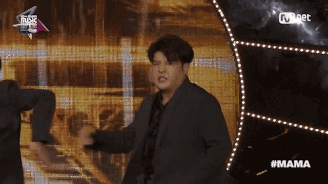 a man in a suit stands on a stage in front of a screen that says mama on it