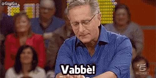 a man with glasses is sitting in front of a crowd and says vabbe