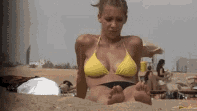 a woman in a yellow bikini is laying in the sand