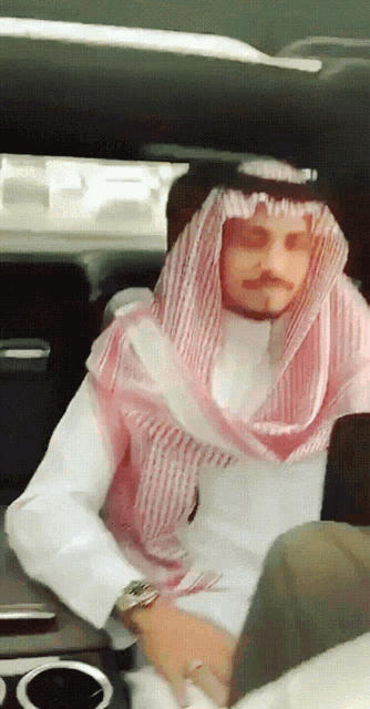 a man wearing a white shirt and a pink and white scarf sits in a car
