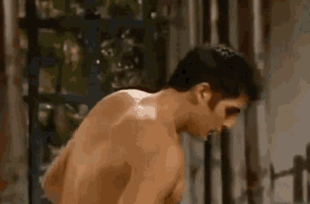 a shirtless man is standing in front of a window looking down .
