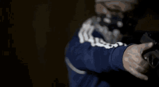a man wearing a bandana and a blue adidas jacket is pointing his finger at the camera .