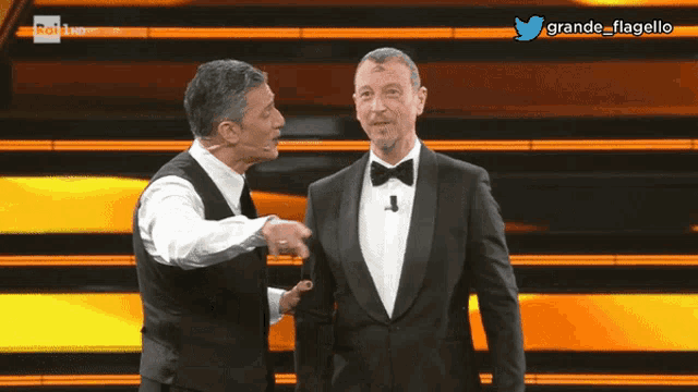 two men in tuxedos are standing on a stage with a twitter icon above them