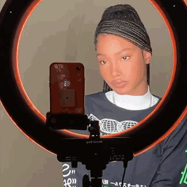 a woman is taking a picture of herself with a ring light behind her