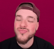 a man with a beard wearing a baseball cap is making a funny face with his eyes closed .