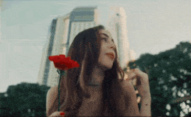 a woman holding a red rose in front of a tall building .