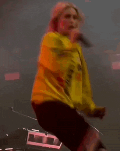 a woman is singing into a microphone while wearing a yellow shirt that says ' u.d.a. '
