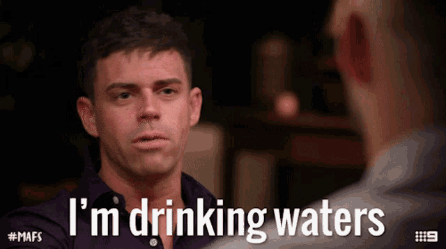 a man in a purple shirt says i 'm drinking waters while talking to another man