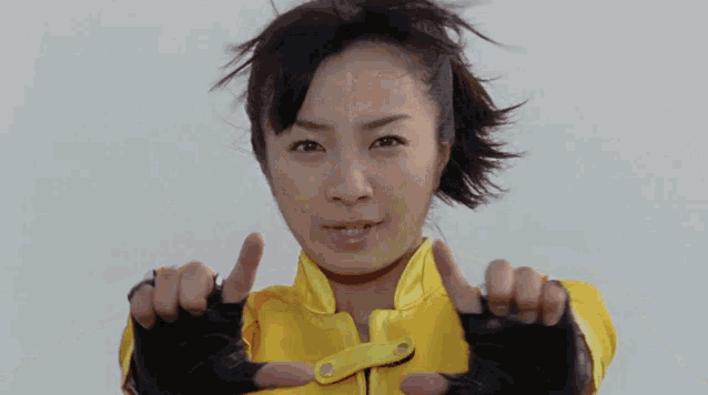 a woman in a yellow jacket and black gloves is making a funny face .