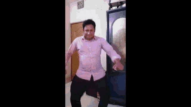 a man in a pink shirt is dancing in a room in front of a mirror .