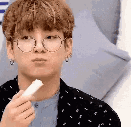 a young man wearing glasses and earrings is holding a piece of food in his hand .