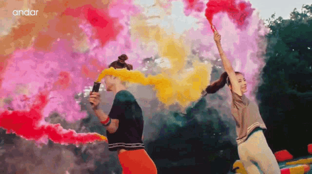 two girls are holding colored smoke bombs and the word andar is visible in the corner