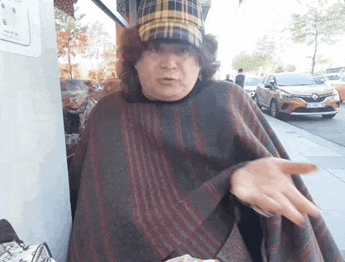 a woman wearing a plaid hat and a poncho stands on a sidewalk in front of a renault car