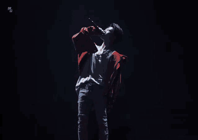 a man in a red jacket is singing into a microphone with the letter l on the bottom right