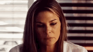 a woman in a white shirt is sitting in front of a window and looking down .