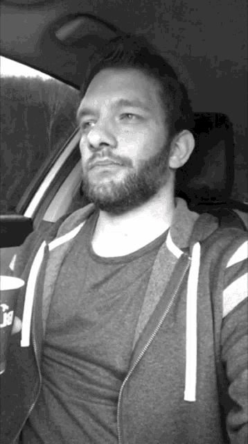 a man with a beard is sitting in a car and holding a cup that says ' a ' on it