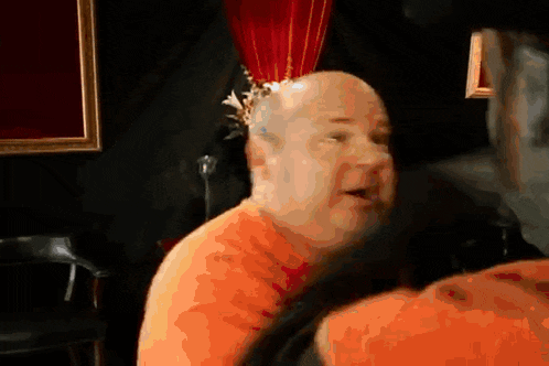a bald man with a crown on his head is looking at something
