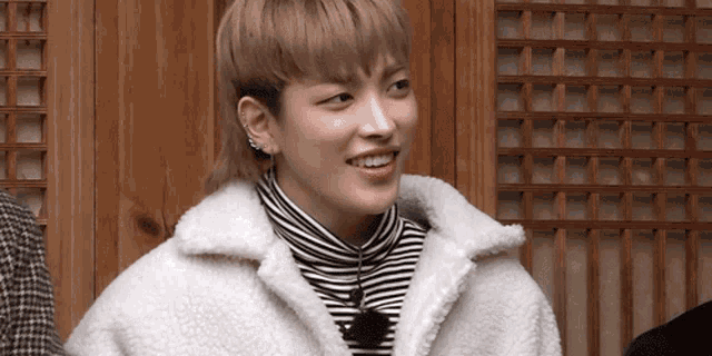 a young man wearing a striped turtleneck and a white jacket is smiling for the camera .