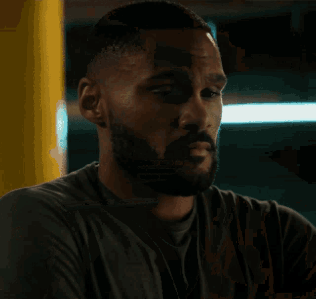 a man with a beard wearing a grey shirt looks over his shoulder