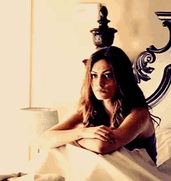 a woman is sitting on a bed with her head resting on her arms .