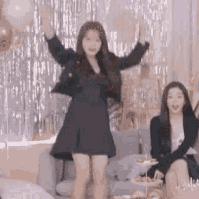 a woman in a black dress is dancing with her arms in the air while sitting on a couch .