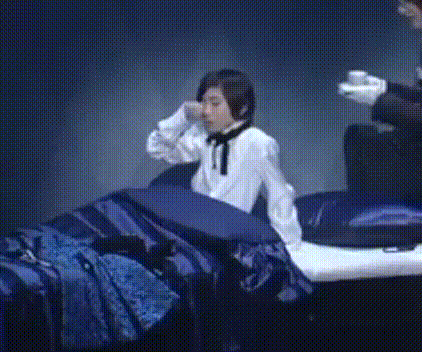 a person in a white shirt and black tie is sitting on a bed with blue sheets .
