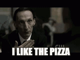 a man in a suit is saying `` i like the pizza '' while holding a pizza .