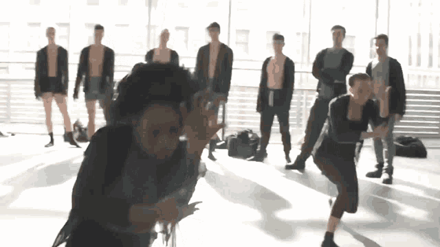 a group of men are standing in a room with a woman dancing