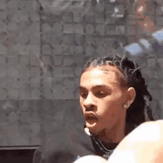 a man with dreadlocks and a tattoo on his forehead is standing in front of a brick wall .